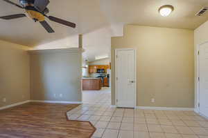 Spare room featuring a ceiling fan, vaulted ceiling, baseboards, light wood-style floors, and a sink