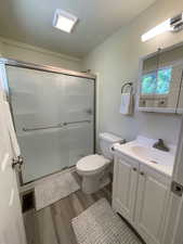Full bath with wood finished floors, a shower stall, toilet, and vanity