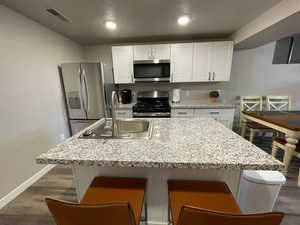 Kitchen featuring appliances with stainless steel finishes, a sink, white cabinets, baseboards, and dark wood-type flooring
