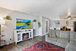 Living room with ceiling fan, wood finished floors, baseboards, and a glass covered fireplace