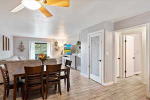 Dining room featuring light wood-style floors, ceiling fan, a textured ceiling, and baseboards