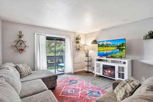 Living area featuring wood finished floors, baseboards, a glass covered fireplace, and a textured ceiling