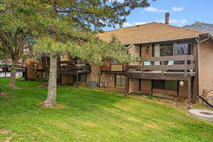 Back of house with a yard, central AC, a balcony, and stucco siding