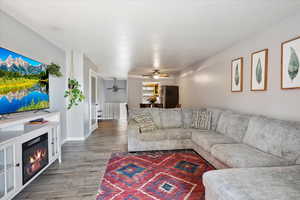 Living area with a ceiling fan, light wood-style floors, a glass covered fireplace, and baseboards