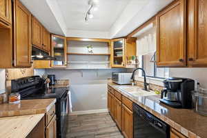 Kitchen featuring black appliances, a sink, under cabinet range hood, open shelves, and brown cabinets