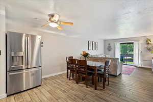 Dining area with light wood-style floors, ceiling fan, baseboards, and a textured ceiling