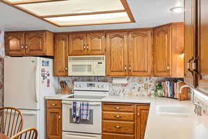 Kitchen with white appliances, a sink, brown cabinets, light countertops, and a textured ceiling