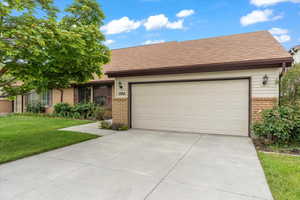 Ranch-style home featuring brick siding, a front yard, driveway, a garage, and a shingled roof