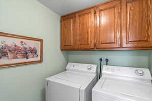 Laundry with cabinet space, separate washer and dryer, and a textured ceiling