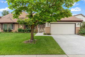 Ranch-style home featuring brick siding, a garage, a front lawn, driveway, and roof with shingles