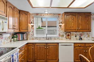 Kitchen with white appliances, a sink, wallpapered walls, brown cabinetry, and light countertops