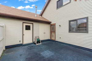 Doorway to property and garage with a patio and a shingled roof