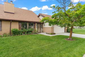 View of front facade with brick siding, driveway, a front yard, roof with shingles, and a chimney