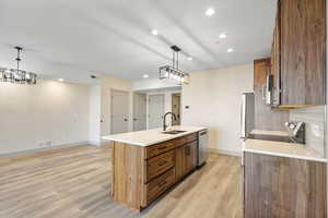 Kitchen with brown cabinets, recessed lighting, an island with sink, pendant lighting, and light wood-style flooring