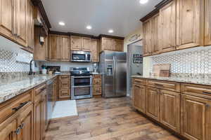 Kitchen with stainless steel appliances, a sink, wood finished floors, decorative backsplash, and recessed lighting