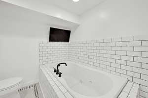 Full bathroom with tile patterned floors, a whirlpool tub, toilet, and baseboards