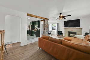 Living area with a fireplace, ceiling fan, light wood finished floors, a textured ceiling, and baseboards