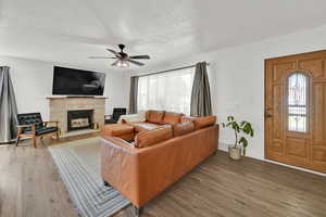 Living room with wood finished floors, a fireplace, ceiling fan, and a textured ceiling