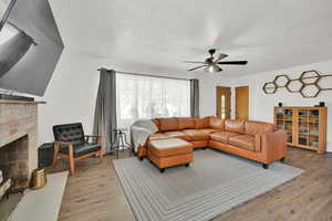 Living area featuring light wood finished floors, a ceiling fan, a brick fireplace, and a textured ceiling