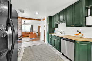 Kitchen featuring freestanding refrigerator, green cabinetry, stainless steel dishwasher, a sink, and decorative backsplash