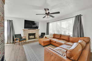 Living room with a fireplace, ceiling fan, a textured ceiling, plenty of natural light, and wood finished floors