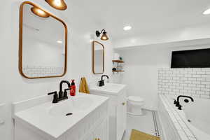 Bathroom with tiled tub, tile patterned floors, two vanities, toilet, and recessed lighting