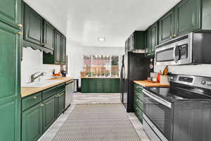 Kitchen with stainless steel appliances, green cabinets, a sink, light wood-style floors, and a textured ceiling