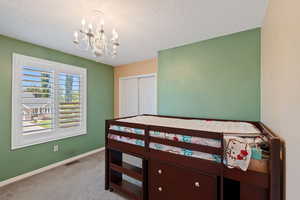 Bedroom with a chandelier, light carpet, baseboards, a textured ceiling, and a closet