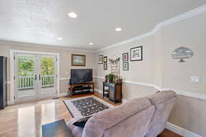 Living room with wood finished floors, french doors, a textured ceiling, ornamental molding, and recessed lighting