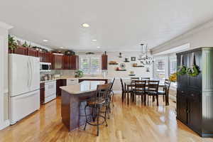 Kitchen with white appliances, light countertops, a textured ceiling, a breakfast bar area, and light wood-style floors