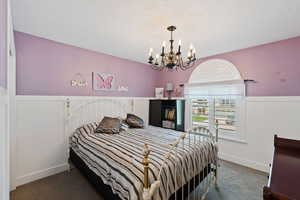 Bedroom featuring a chandelier, carpet, a wainscoted wall, a textured ceiling, and baseboards