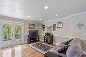 Living room with light wood finished floors, a textured ceiling, french doors, recessed lighting, and crown molding