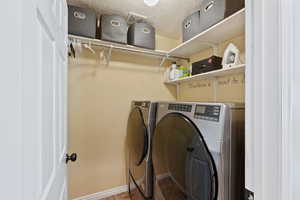 Washroom featuring washing machine and clothes dryer, a textured ceiling, and baseboards