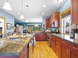 Kitchen featuring stainless steel appliances,  sink, light wood-type flooring, and pendant lighting with stone counters