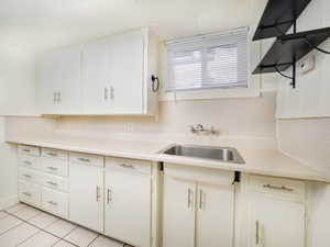 Kitchen with light countertops, light tile patterned floors, white cabinetry, and a sink
