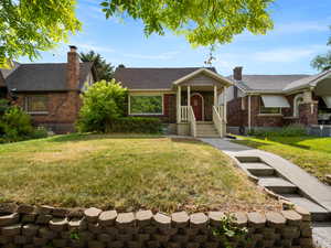 View of front facade with a front lawn, brick siding, roof with shingles, and a chimney