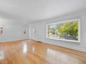 Foyer entrance with light wood finished floors, baseboards, visible vents, and a textured ceiling