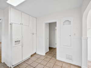Interior space with a wainscoted wall, arched walkways, visible vents, white cabinetry, and white fridge with ice dispenser
