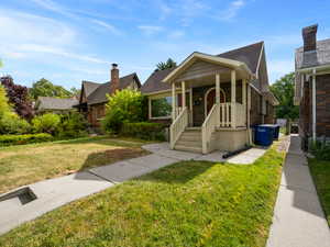 Bungalow-style home with a front lawn, brick siding, roof with shingles, and a chimney