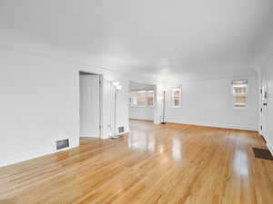 Unfurnished living room featuring light wood finished floors, baseboards, and visible vents