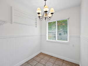 Empty room with a wainscoted wall, a wealth of natural light, and a notable chandelier