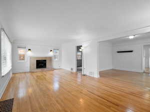 Unfurnished living room with a tiled fireplace, light wood-style flooring, and visible vents