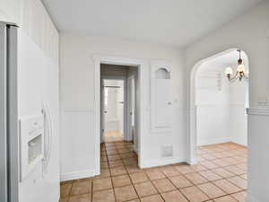 Interior space with wainscoting, light tile patterned flooring, arched walkways, an inviting chandelier, and visible vents