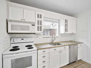 Kitchen featuring white cabinets, glass insert cabinets, a sink, and white appliances
