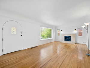 Unfurnished living room with a tile fireplace, light wood-style flooring, visible vents, and a wealth of natural light