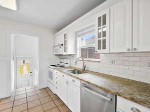 Kitchen with white cabinets, a sink, glass insert cabinets, decorative backsplash, and white appliances