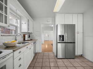 Kitchen with appliances with stainless steel finishes, white cabinets, tasteful backsplash, and glass insert cabinets