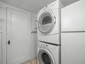 Washroom with stacked washer and clothes dryer and light tile patterned floors