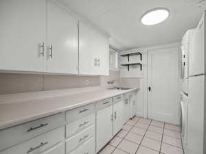 Kitchen with stacked washer and clothes dryer, light tile patterned floors, light countertops, and white cabinetry