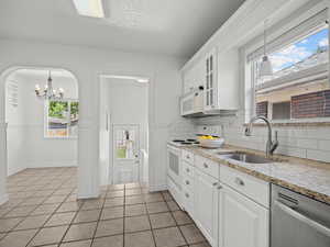 Kitchen with white appliances, light tile patterned flooring, a chandelier, decorative backsplash, and white cabinets